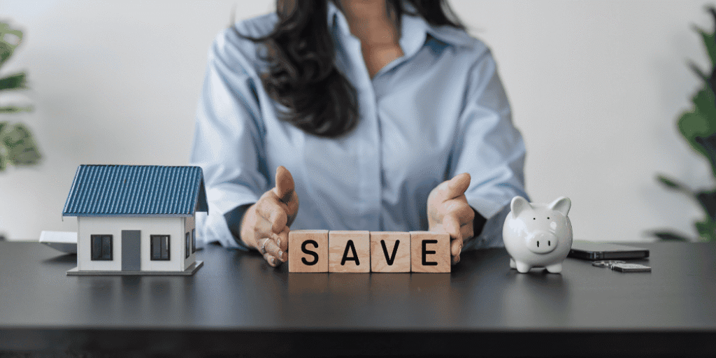 Woman at desk with piggy bank, house model, and wooden blocks spelling SAVE