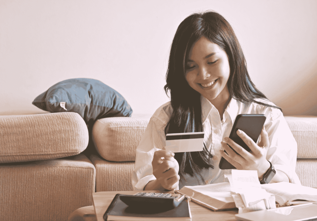 Woman paying bills online using her phone and credit card as part of automated bill payments.