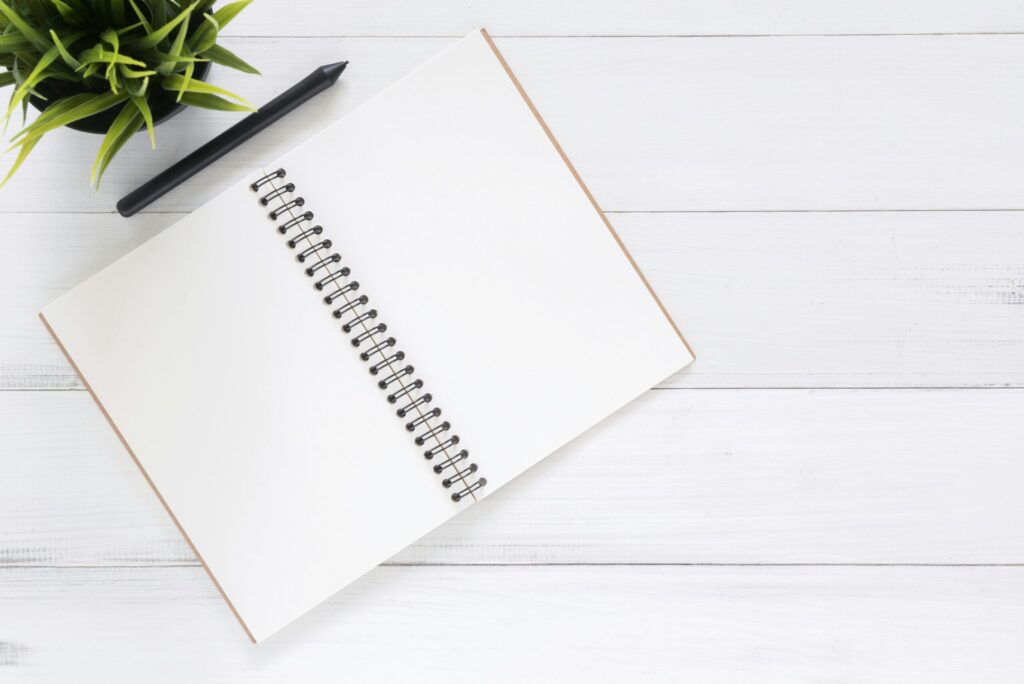 Flatlay of an open notebook with a plant on a white desk, used to represent budgeting tools for Canadians.