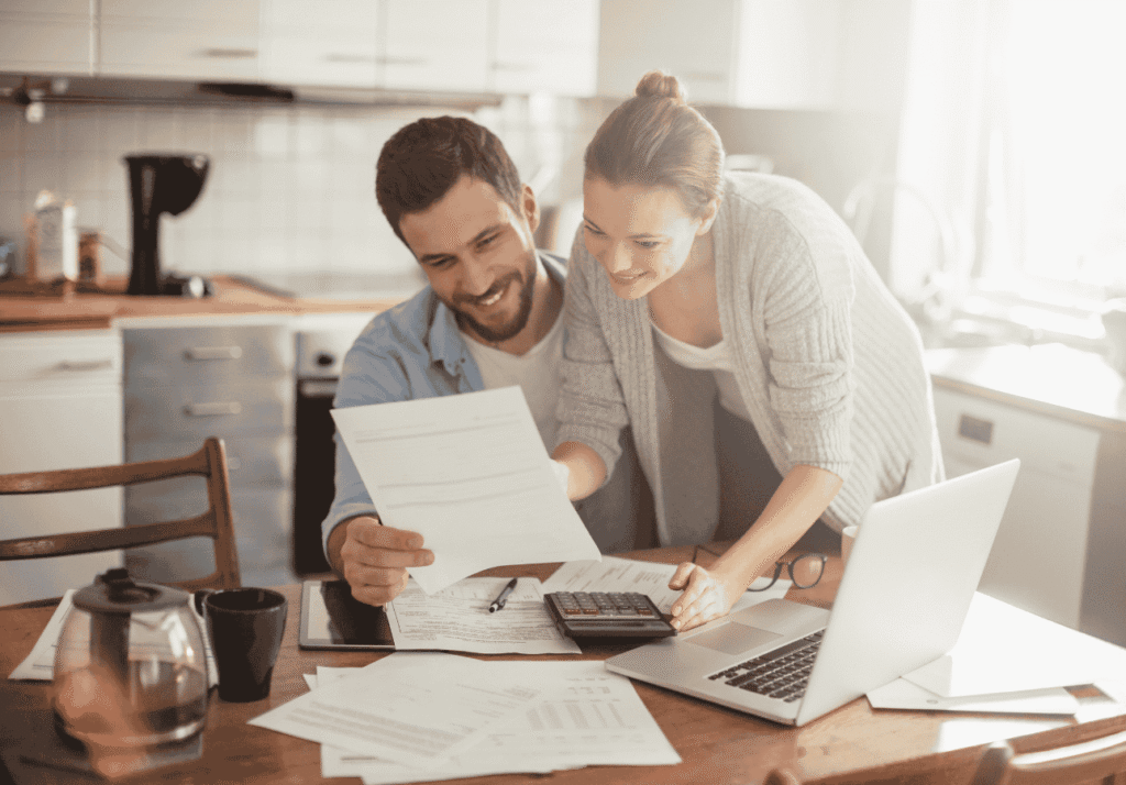 Couple reviewing household bills together at the kitchen table with a laptop and calculator.