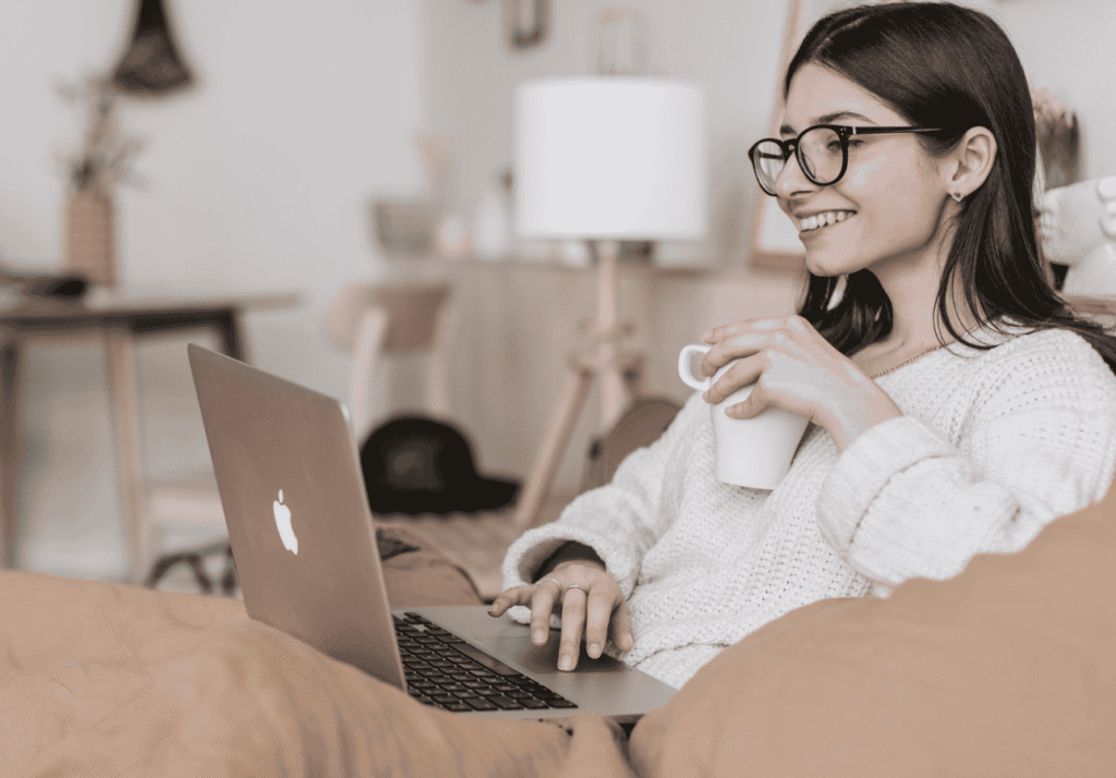 Woman using a laptop and drinking coffee while managing her digital banking from home.