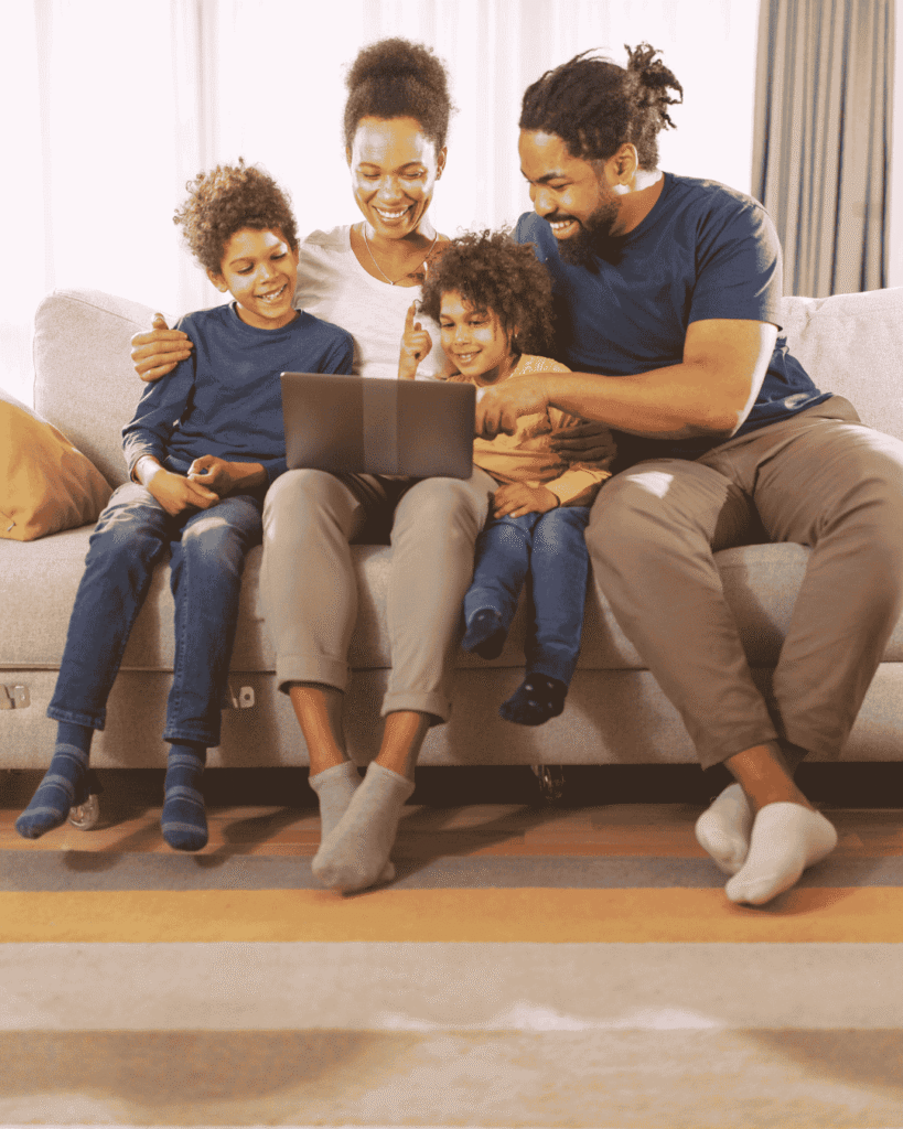 A family sitting together on the couch using a laptop, representing families choosing the best no-fee credit cards in Canada.