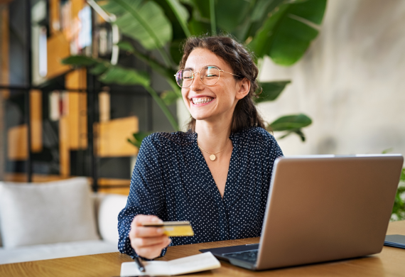 Smiling woman holding a credit card while shopping online with her laptop.