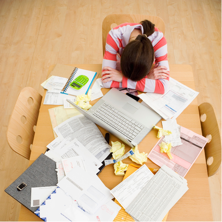 Person overwhelmed by bills and paperwork at a desk, illustrating financial stress caused by too many money decisions
