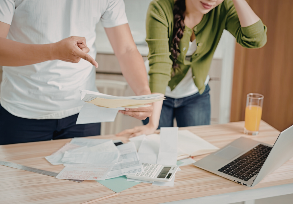 Canadian couple reviewing bills and finances at home with laptop, calculator, and paperwork on table