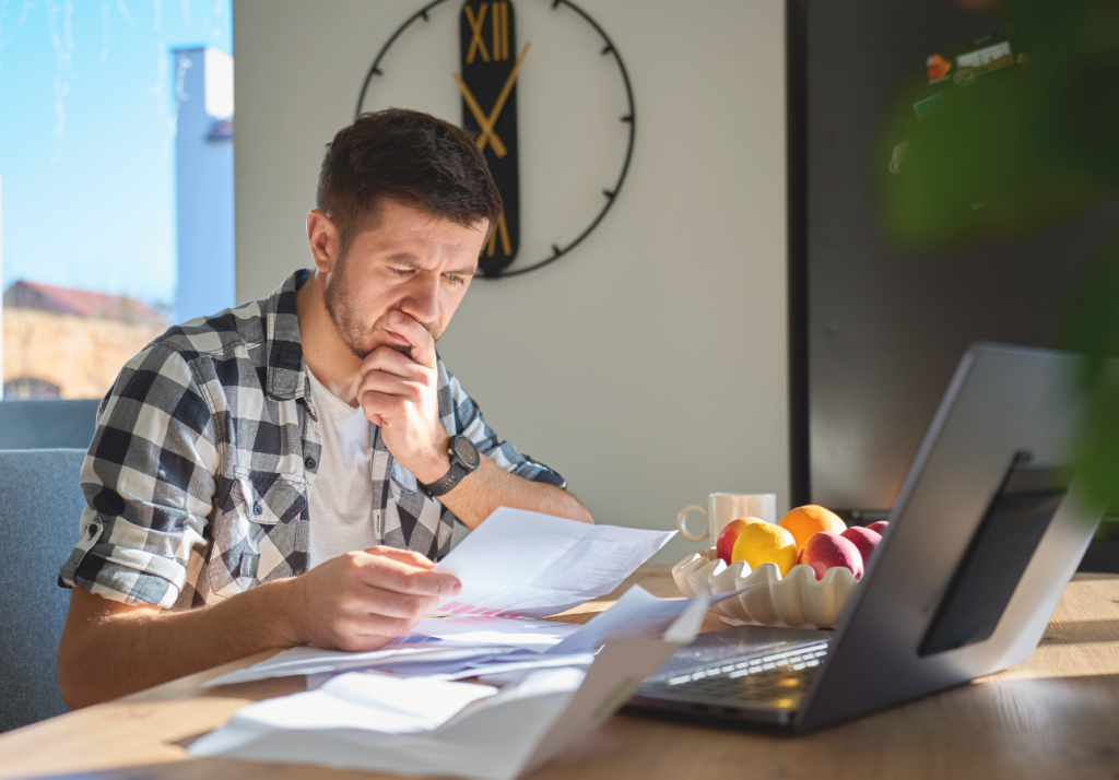 Man reviewing financial documents and bills at home with a laptop, representing tax planning and managing personal finances in Canada