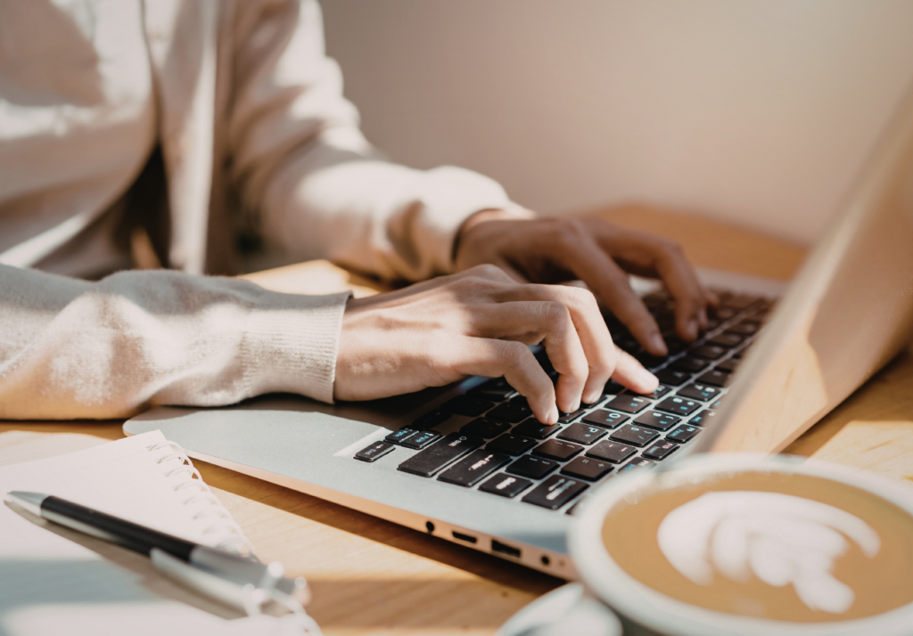 Person typing on laptop planning investments at home with notebook and coffee